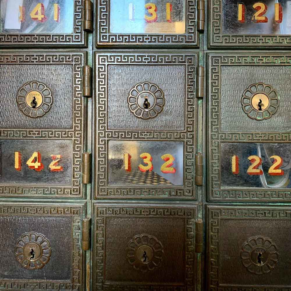 A wall of small antique post office boxes, each with a handpainted number. The box in the center is numbered 132.