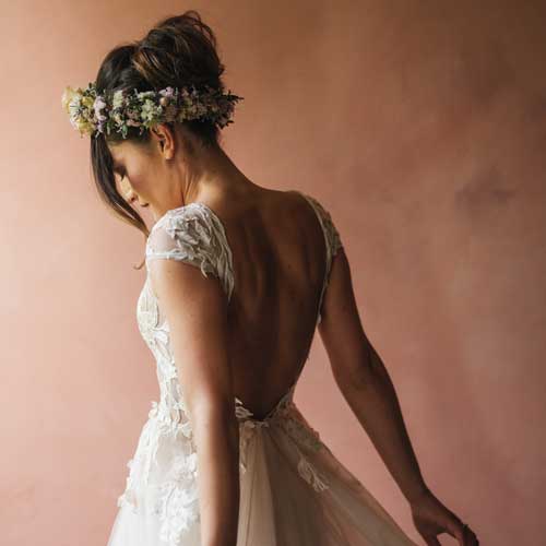 A bride wearing a lace dress and fresh flower crown takes a moment to gather herself in front of a terracotta wall.
