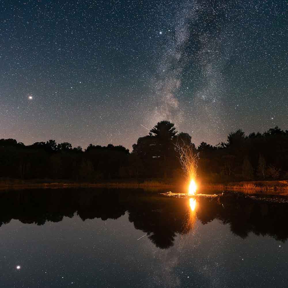 A campfire burns on the shores of a quarry pond